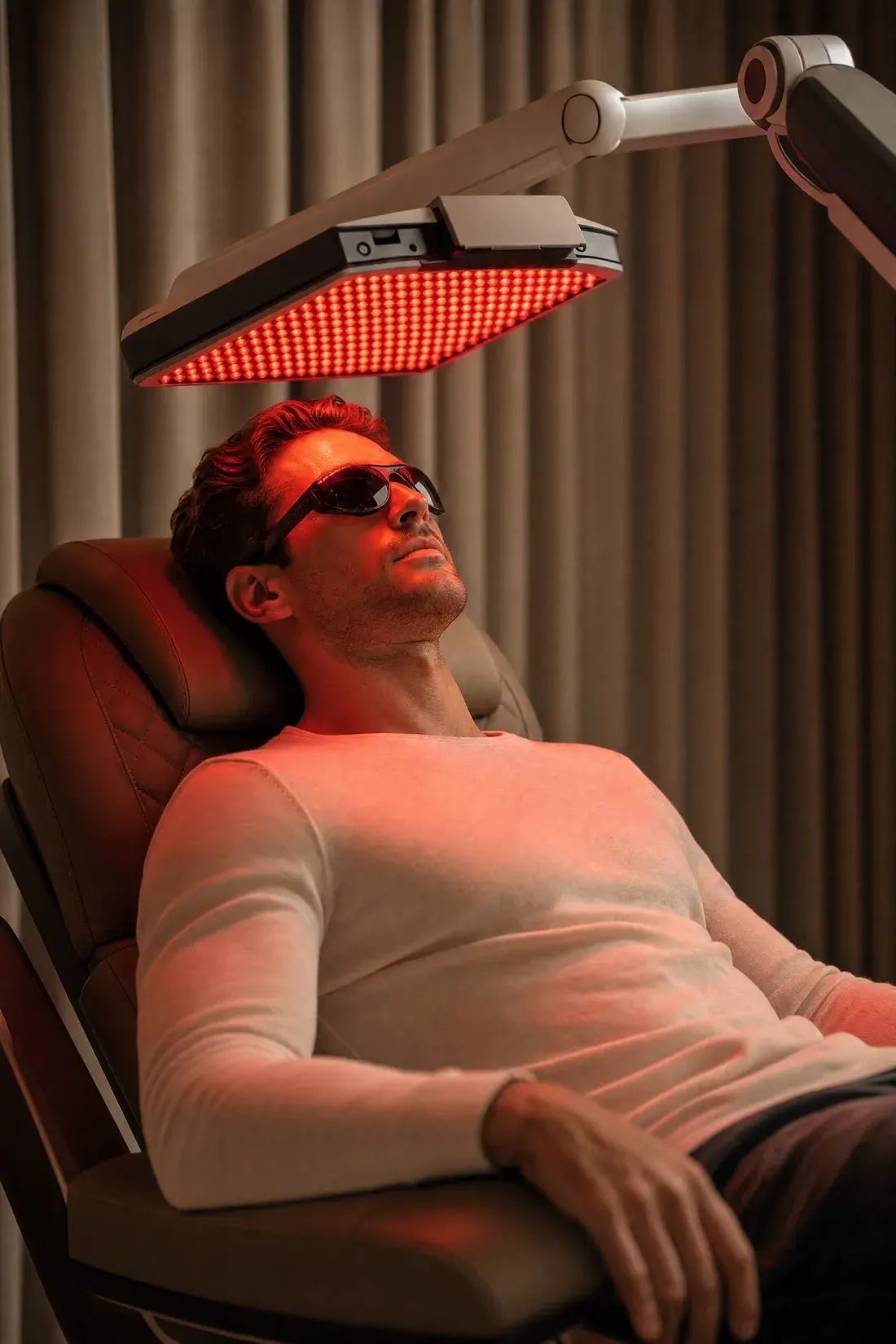 A person reclining under a clinical LED light-therapy panel