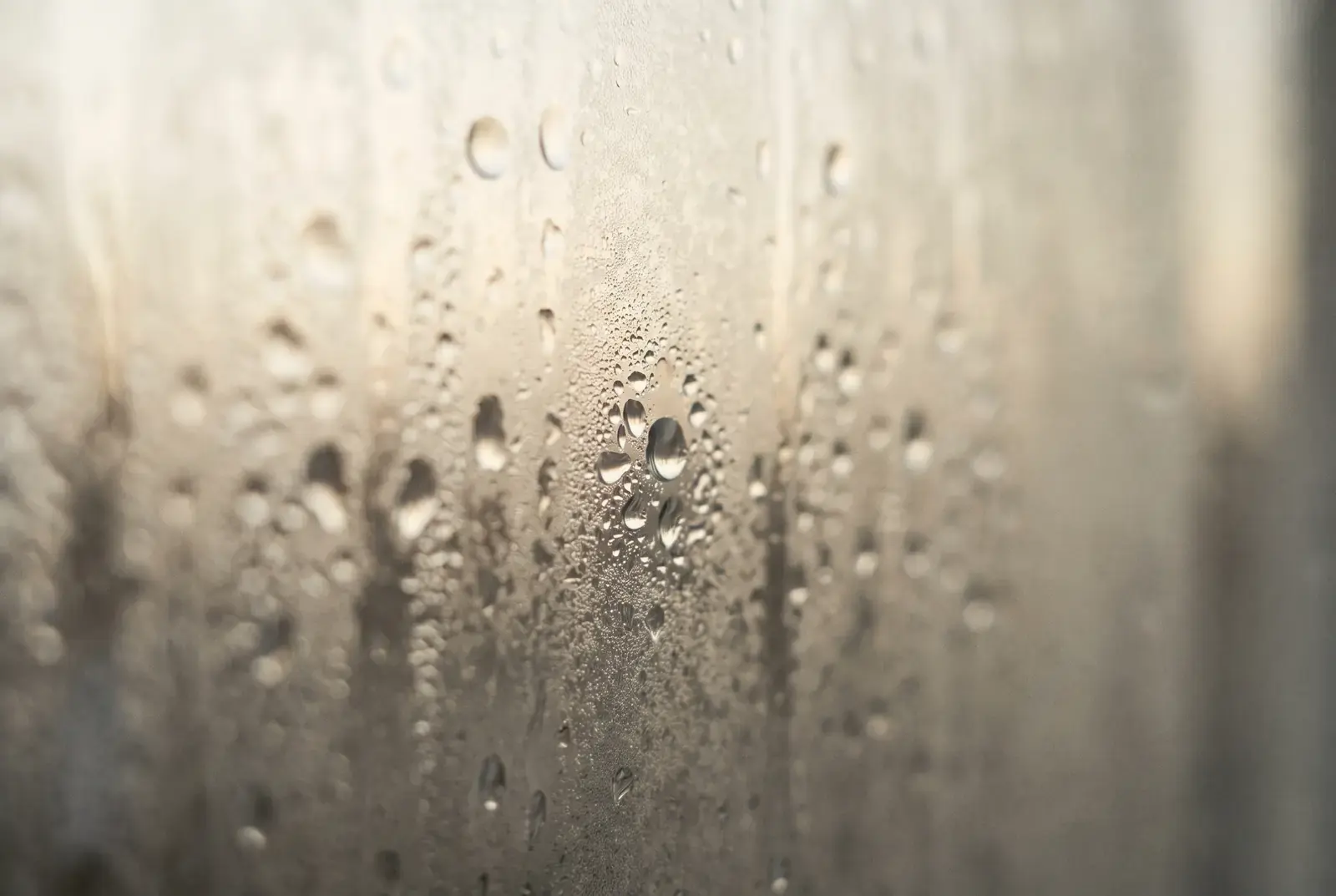 Heavy condensation on a warm-toned pane of glass, everything beyond it softened and indistinct