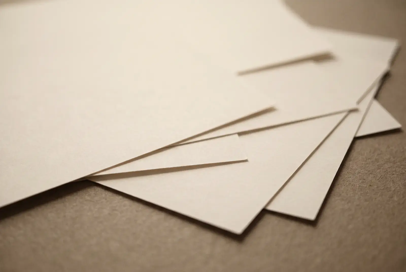 Several loose sheets of warm off-white paper overlapping on a pale surface, almost but not quite aligned