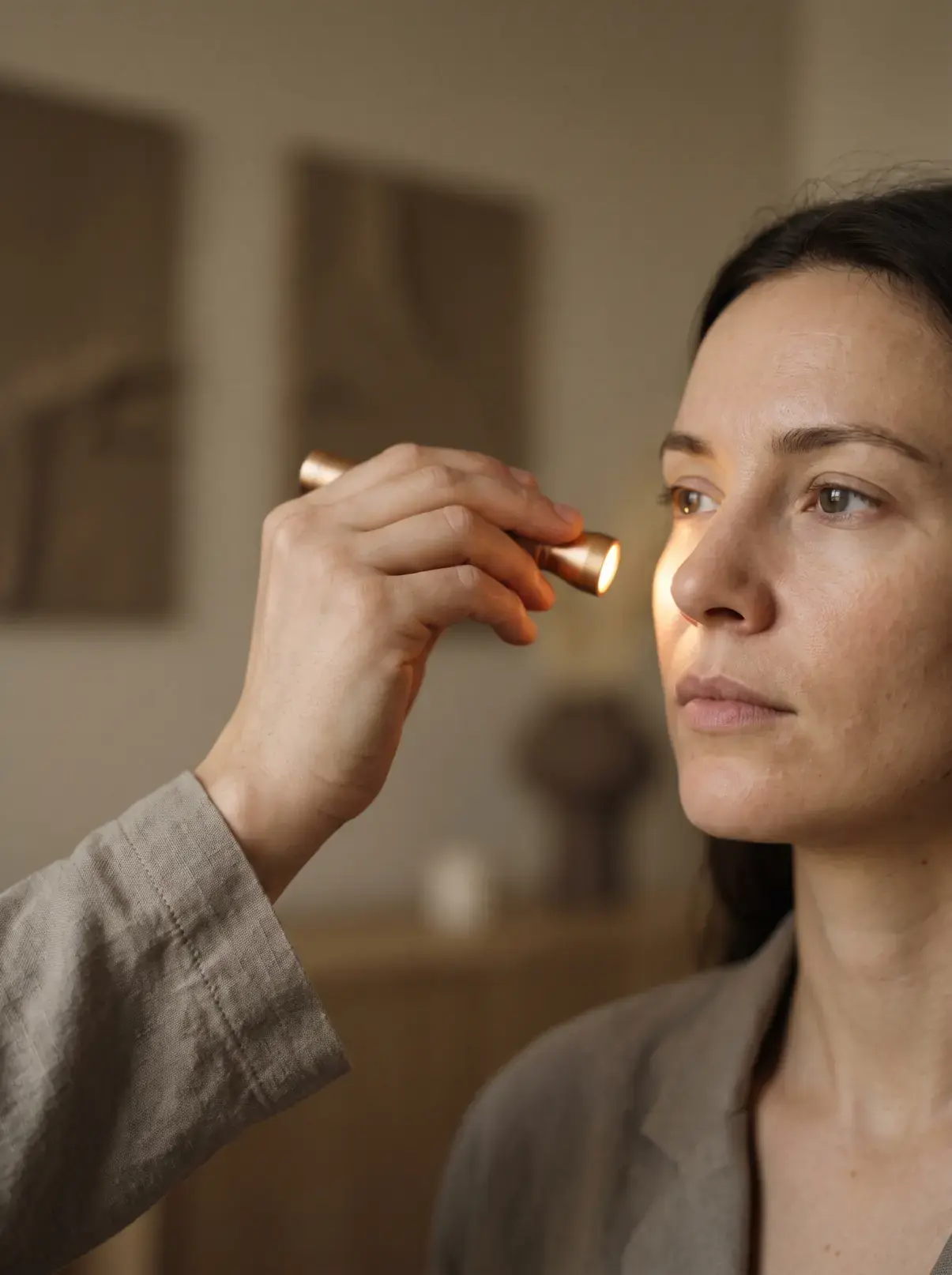 A practitioner holding a small light at a low angle against a client's cheek to read the skin's surface texture
