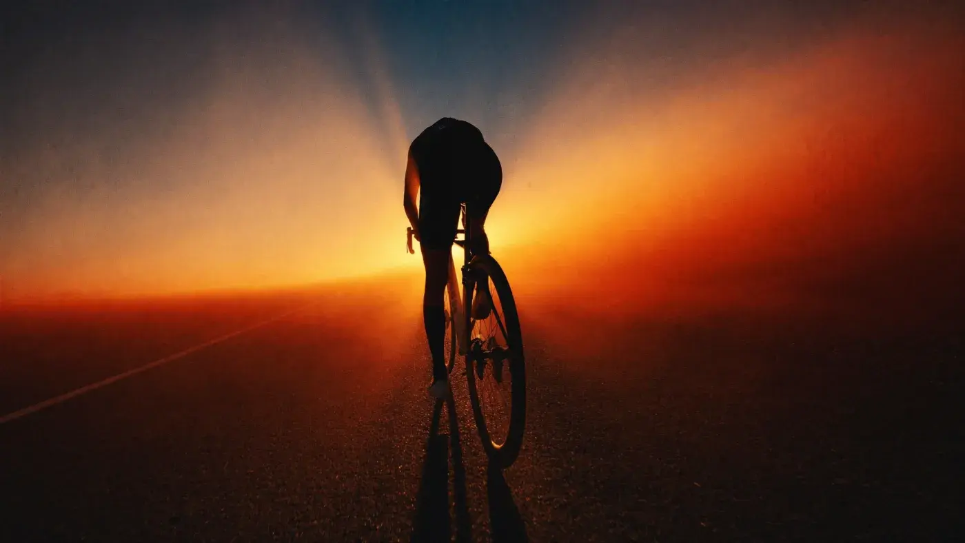 A road cyclist in silhouette against sunrise on an open desert highway