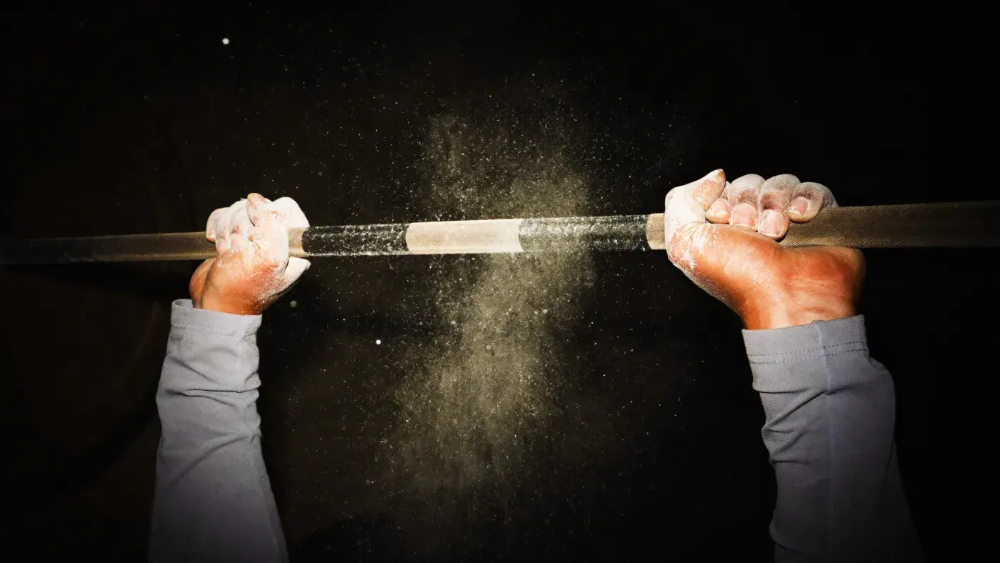 Chalked hands gripping a loaded barbell in a haze of chalk dust