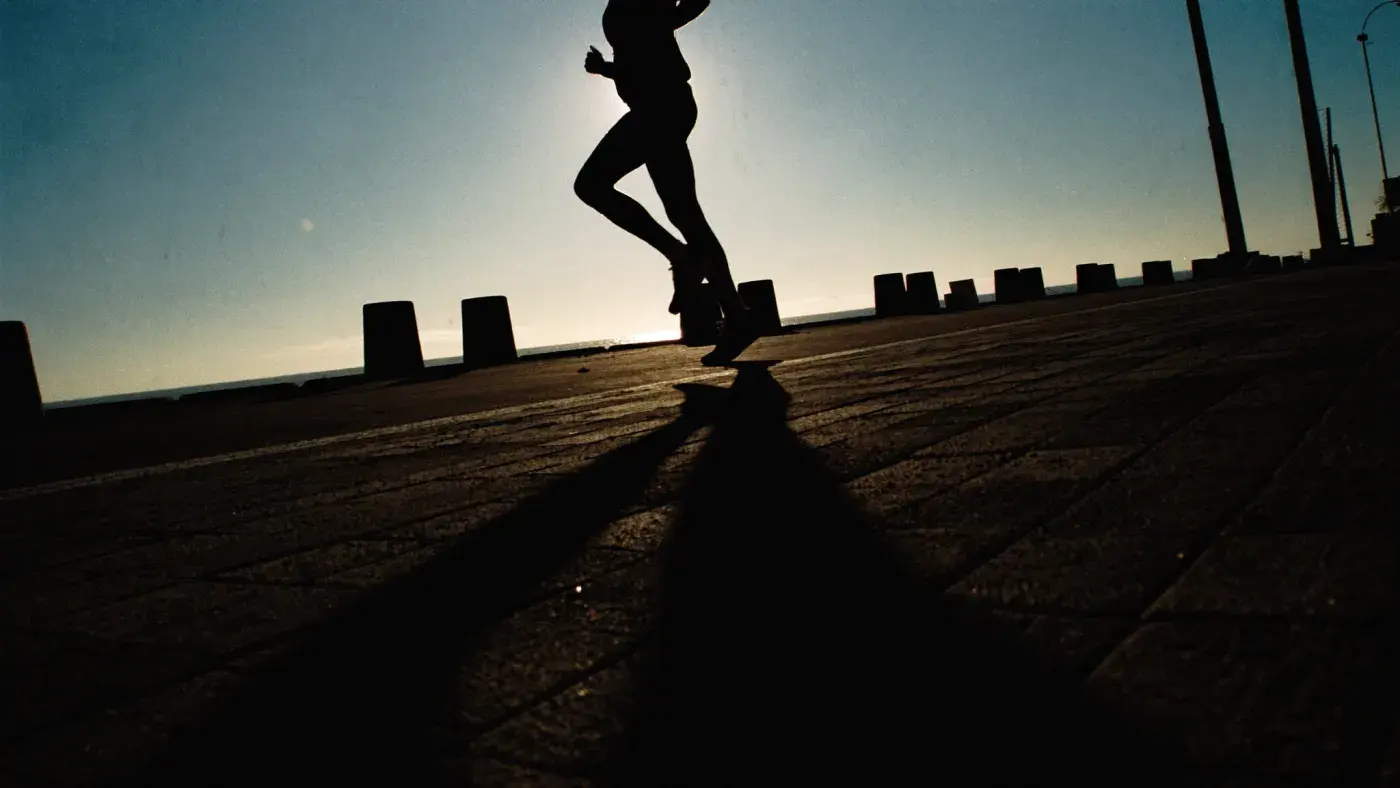 A runner in silhouette against low sunrise light on a coastal promenade