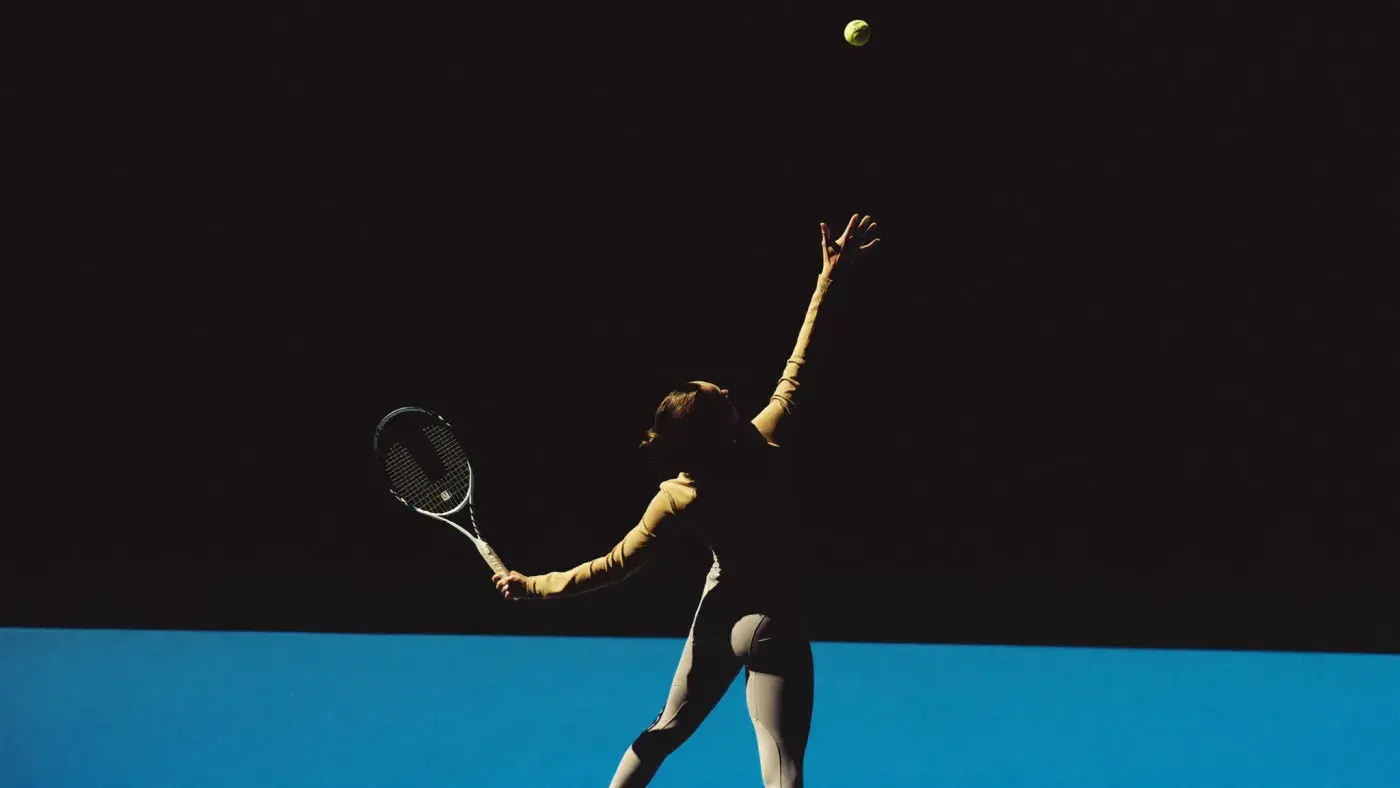 A tennis player in silhouette at full extension in the serve position